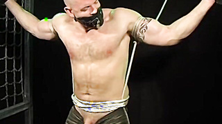 Bigg Pette has his arms trussed with leather and his nutsack tied down to his toes
